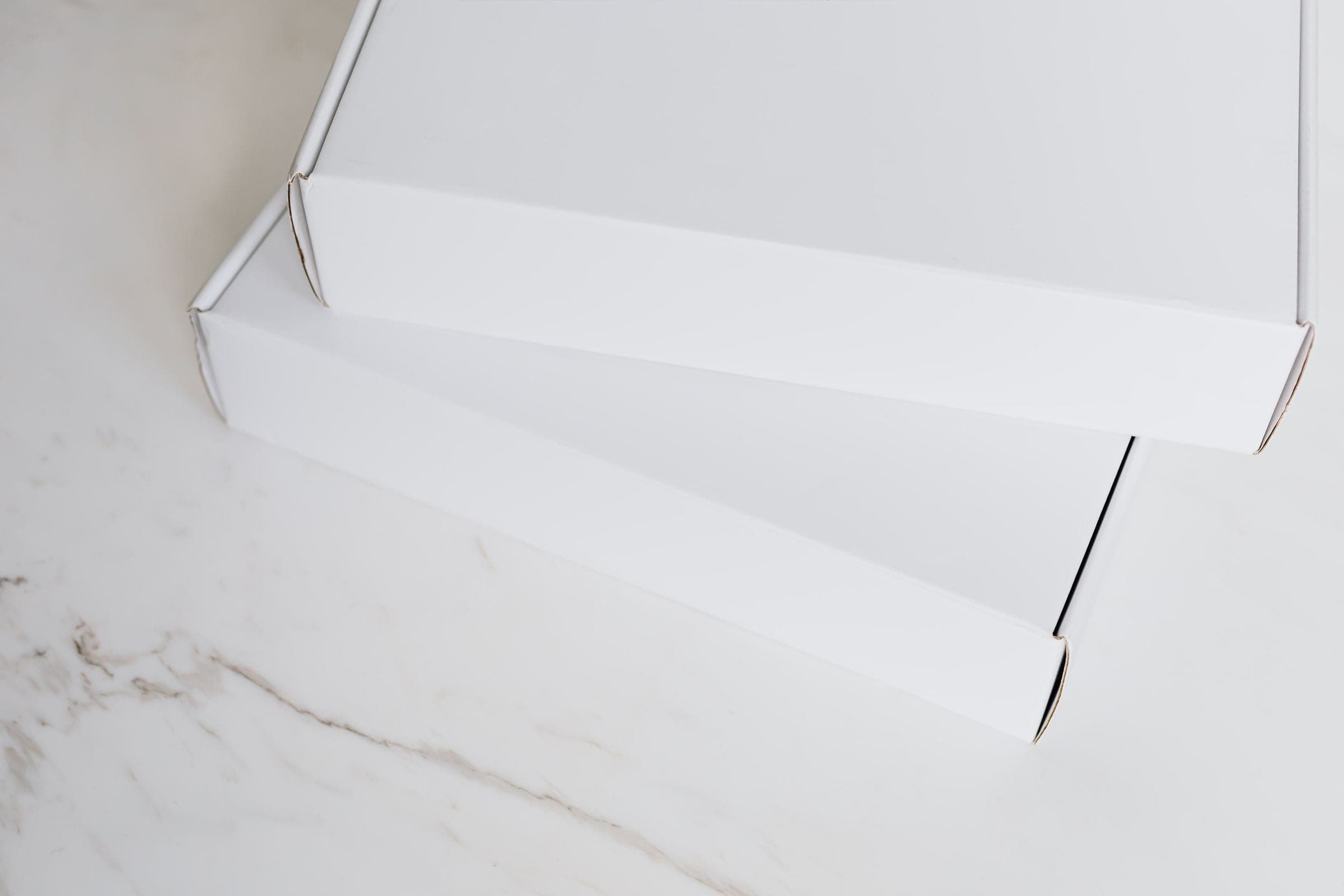 Two plain white shipping boxes stacked on a white marble surface