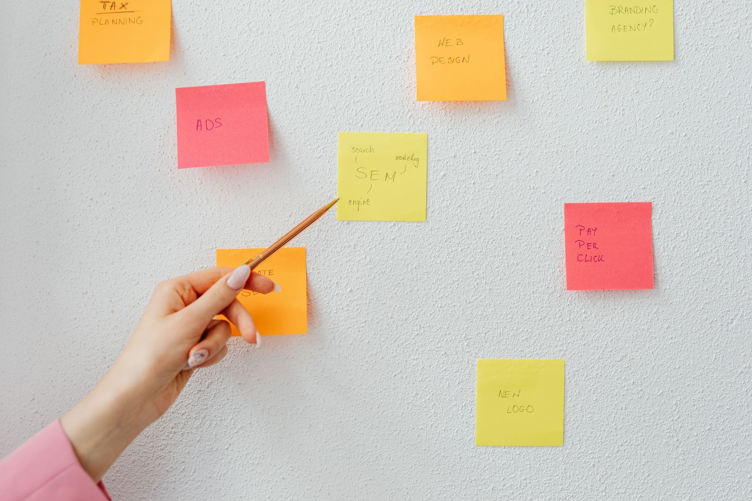 Hand pointing a pen at sticky notes about ads, SEM, web design and a new logo